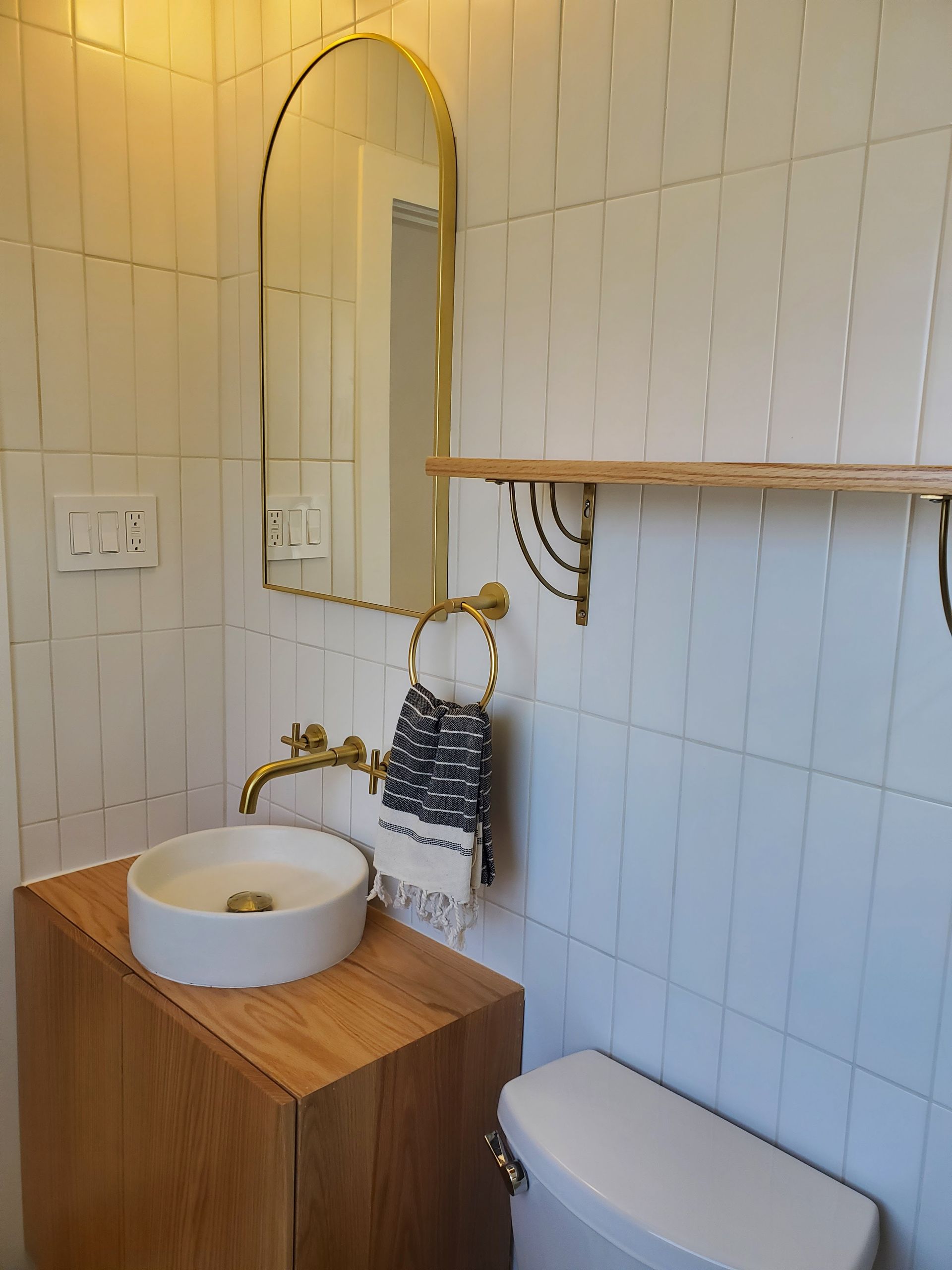 A bathroom with a sink , toilet , mirror and shelf.