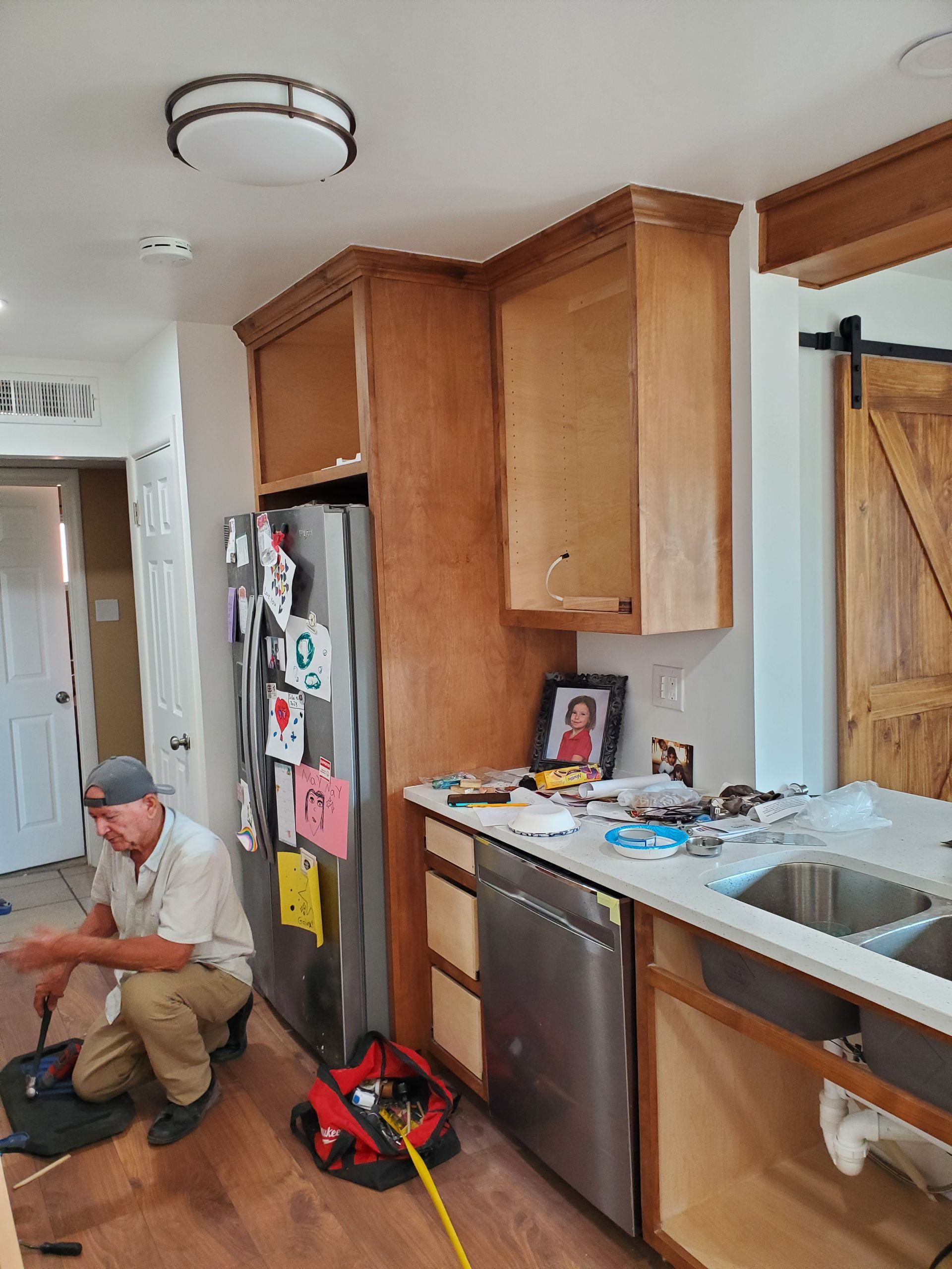 A man is kneeling in a kitchen working on a refrigerator.