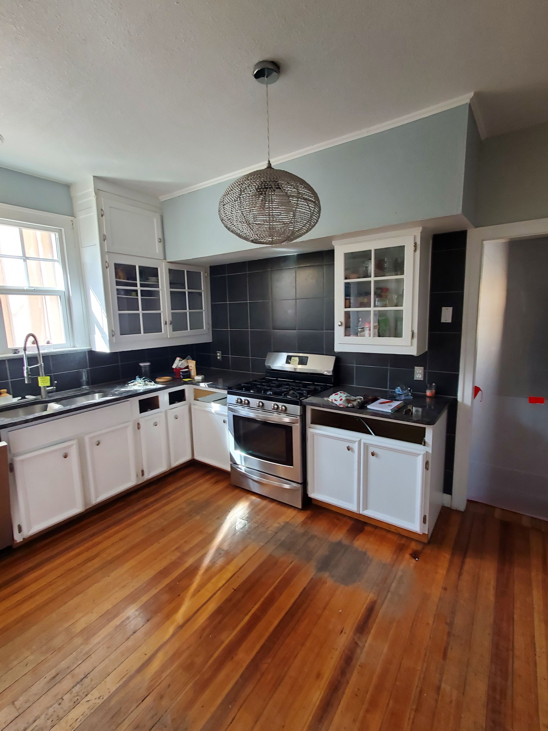 A kitchen with wooden floors , white cabinets , a stove and a sink.