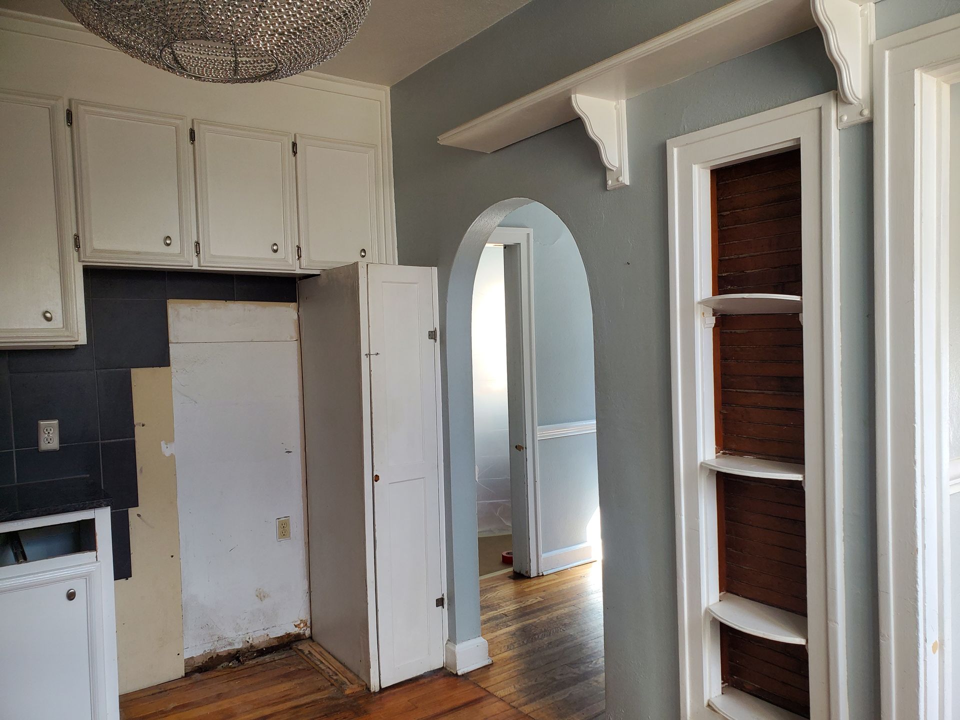 An empty kitchen with white cabinets and a chandelier hanging from the ceiling.