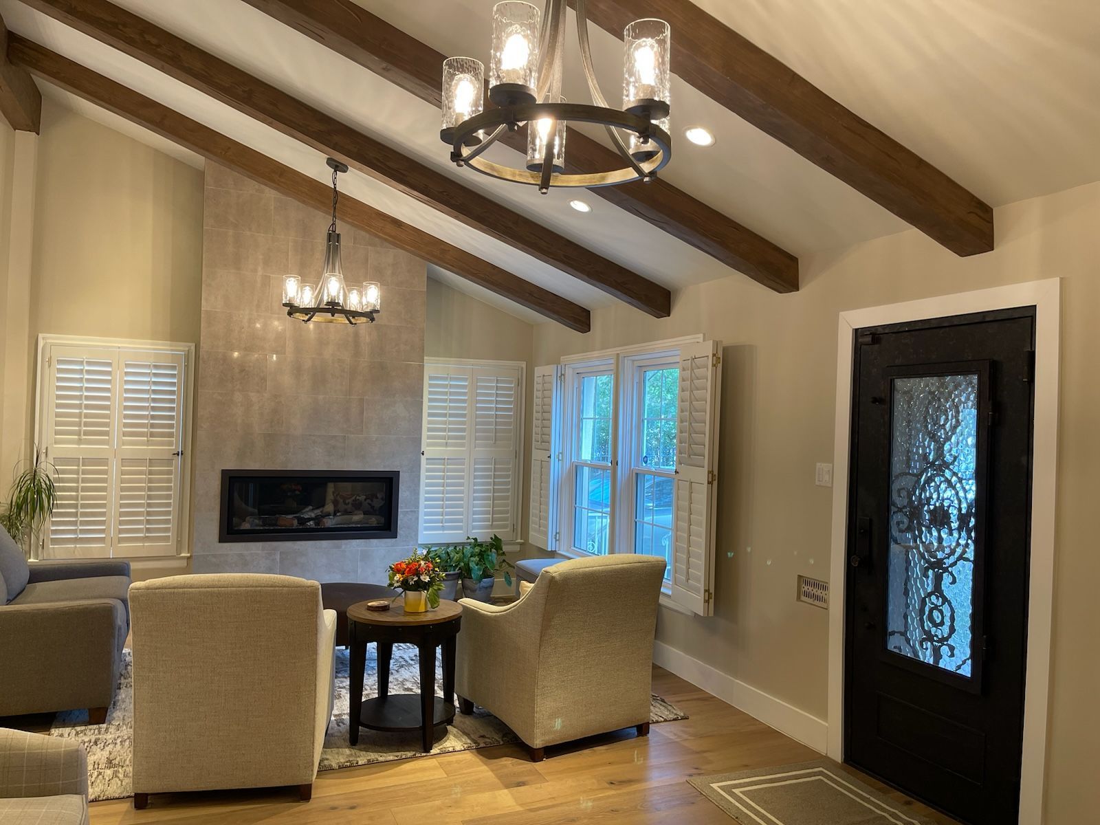 A living room with a fireplace , chairs , a table and a chandelier.