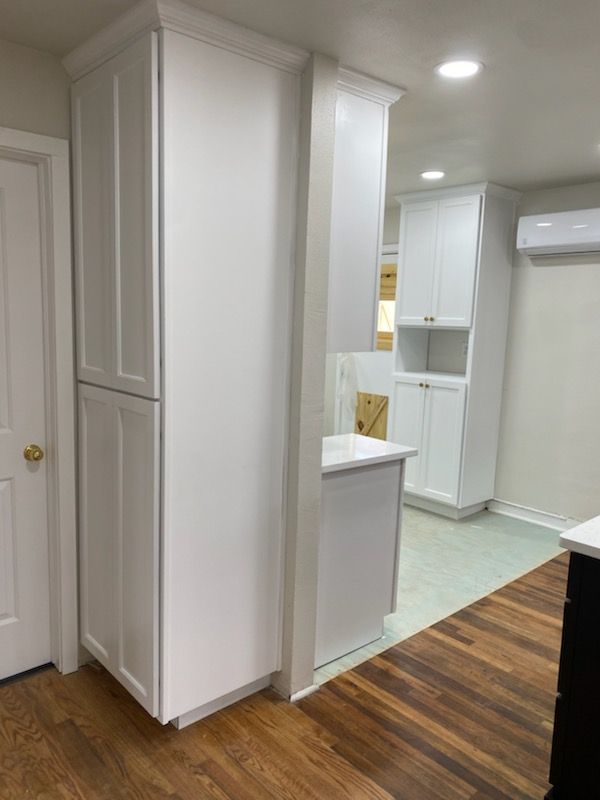 A kitchen with white cabinets and hardwood floors.