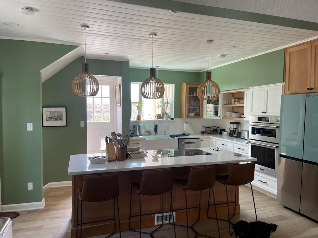 A kitchen with green walls , white cabinets , stainless steel appliances and a large island.