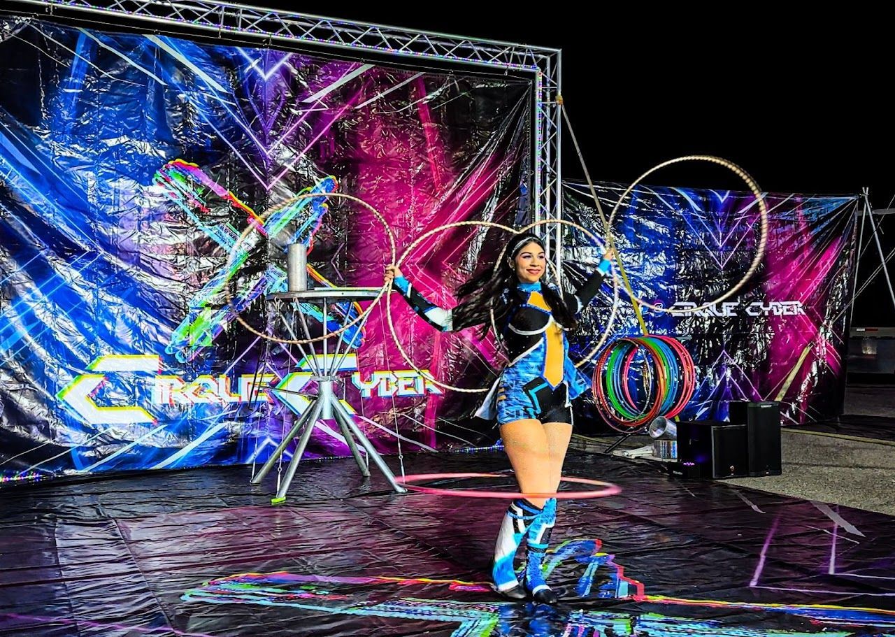 Woman on a neon-lit stage with colorful abstract backdrop and hoop props, posing in a blue outfit