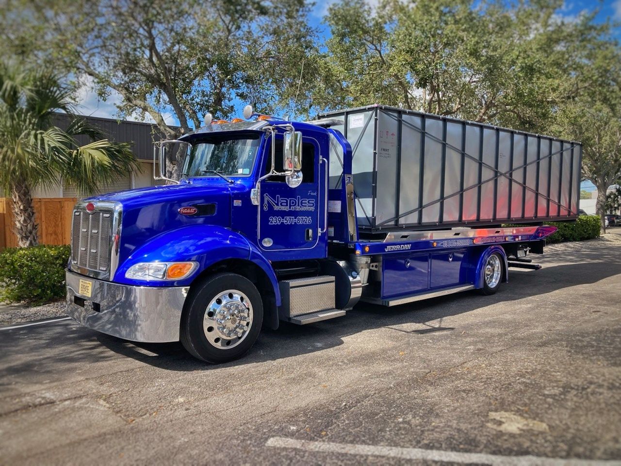 Blue semi-truck with a large trailer parked on a sunny street.
