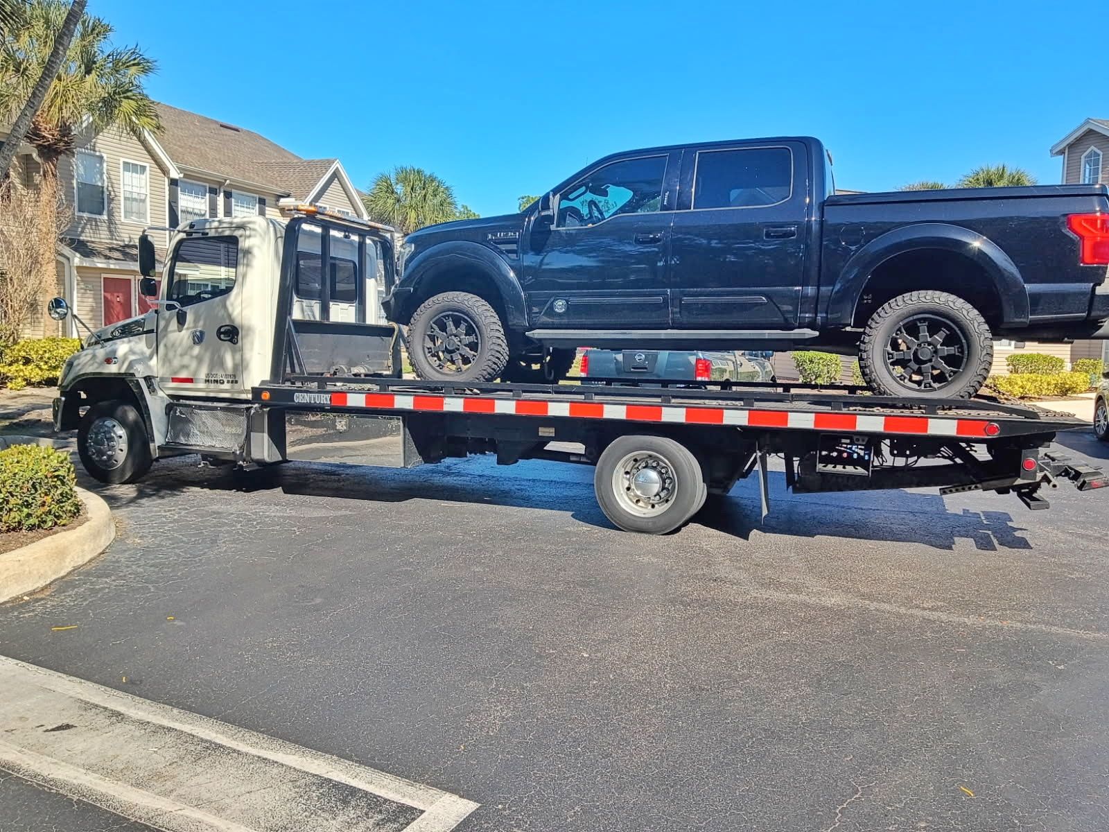 Tow truck carrying a black pickup on a flatbed trailer in a neighborhood street