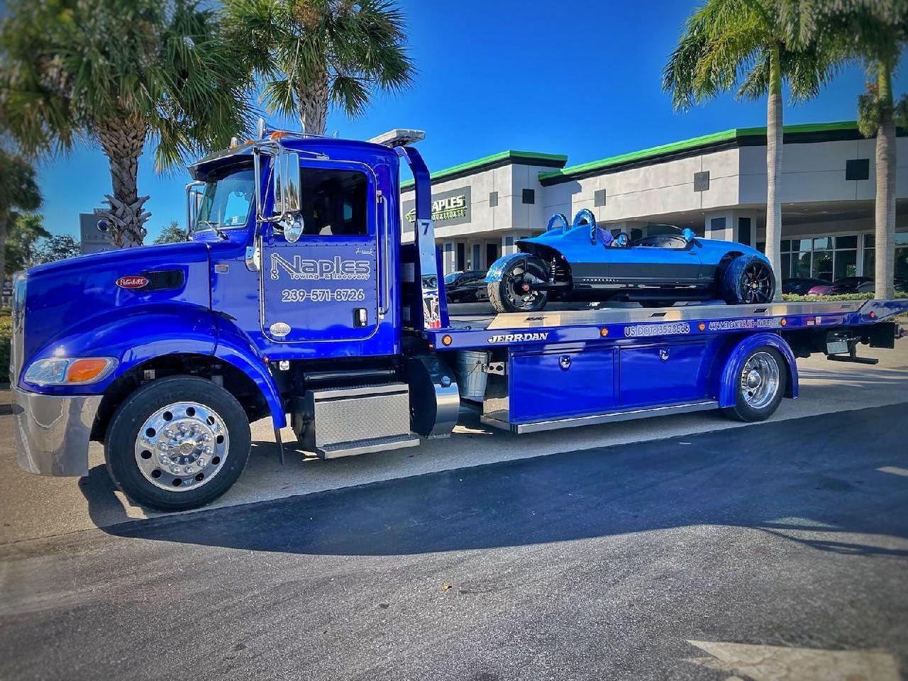 Blue car carrier truck hauling a blue sports car on a sunny street near palm trees