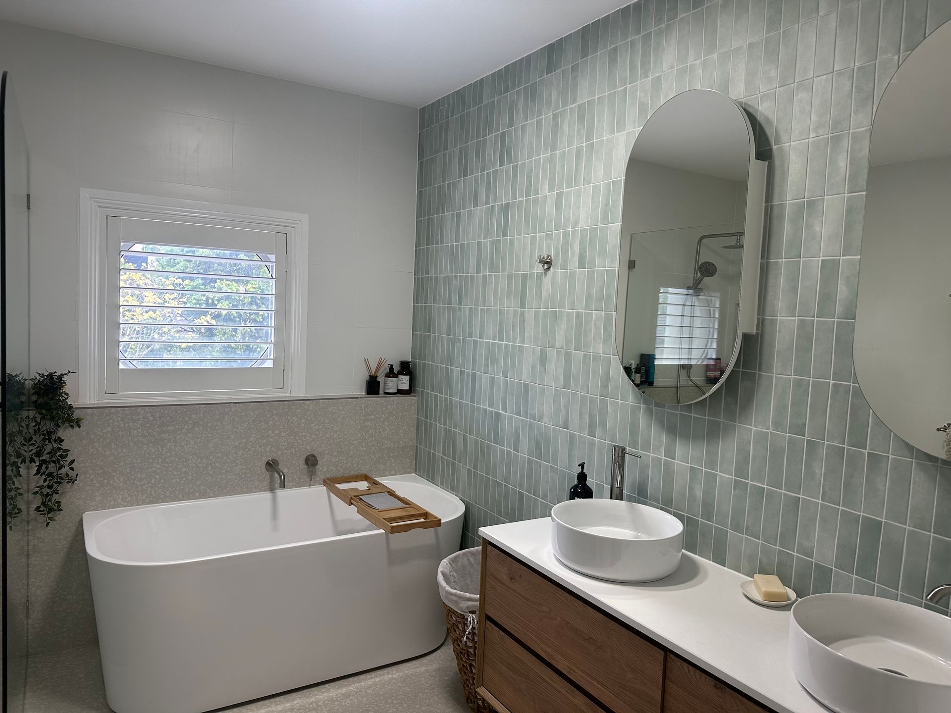 A bathroom with a bathtub , sink , mirror and window.