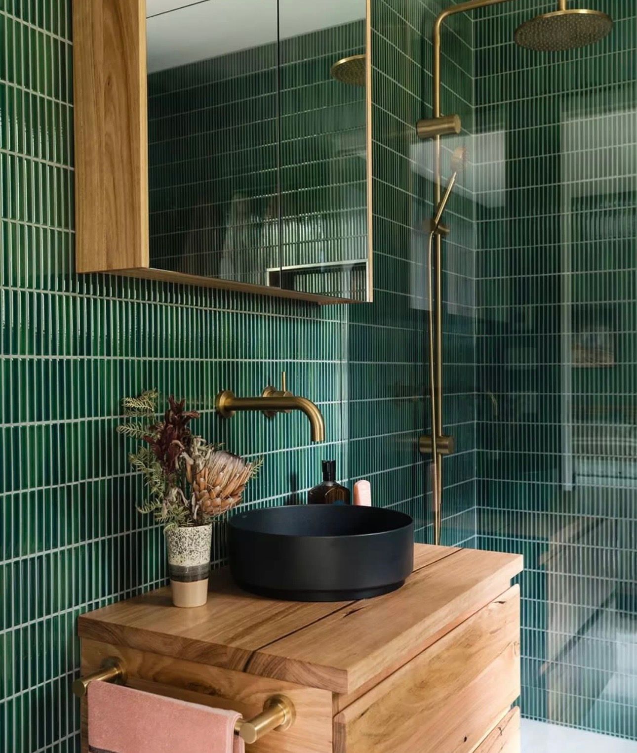 A bathroom with green tiles , a sink , a mirror and a shower.