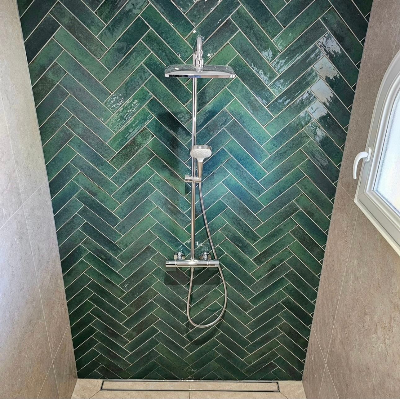 A shower with green tiles on the wall and a window.