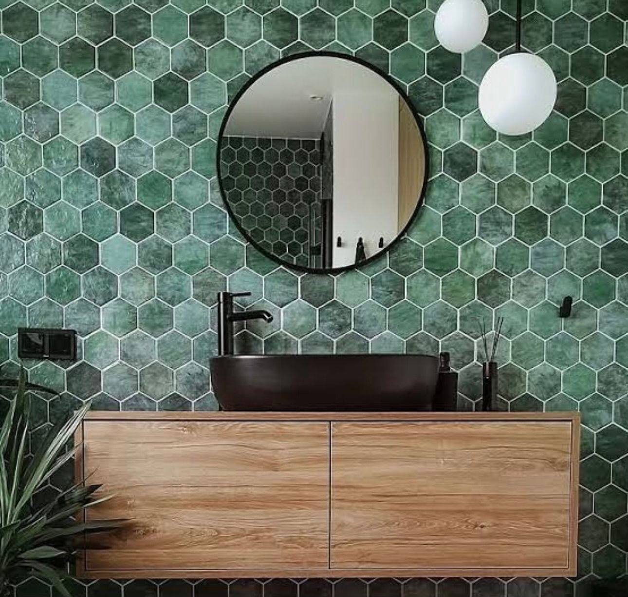 A bathroom with green tiles , a sink , a mirror and a wooden cabinet.