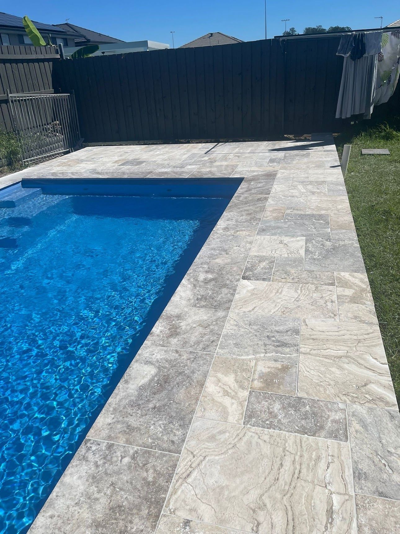 A swimming pool with a tiled walkway and a fence in the background.