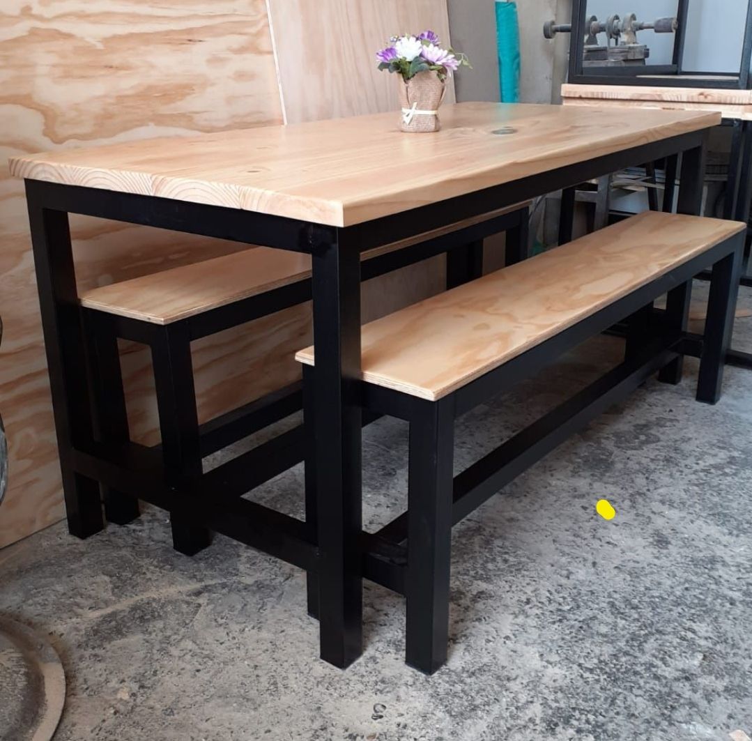 Mesa de madera con marco negro y banco a juego en un taller o sala de exposiciones.