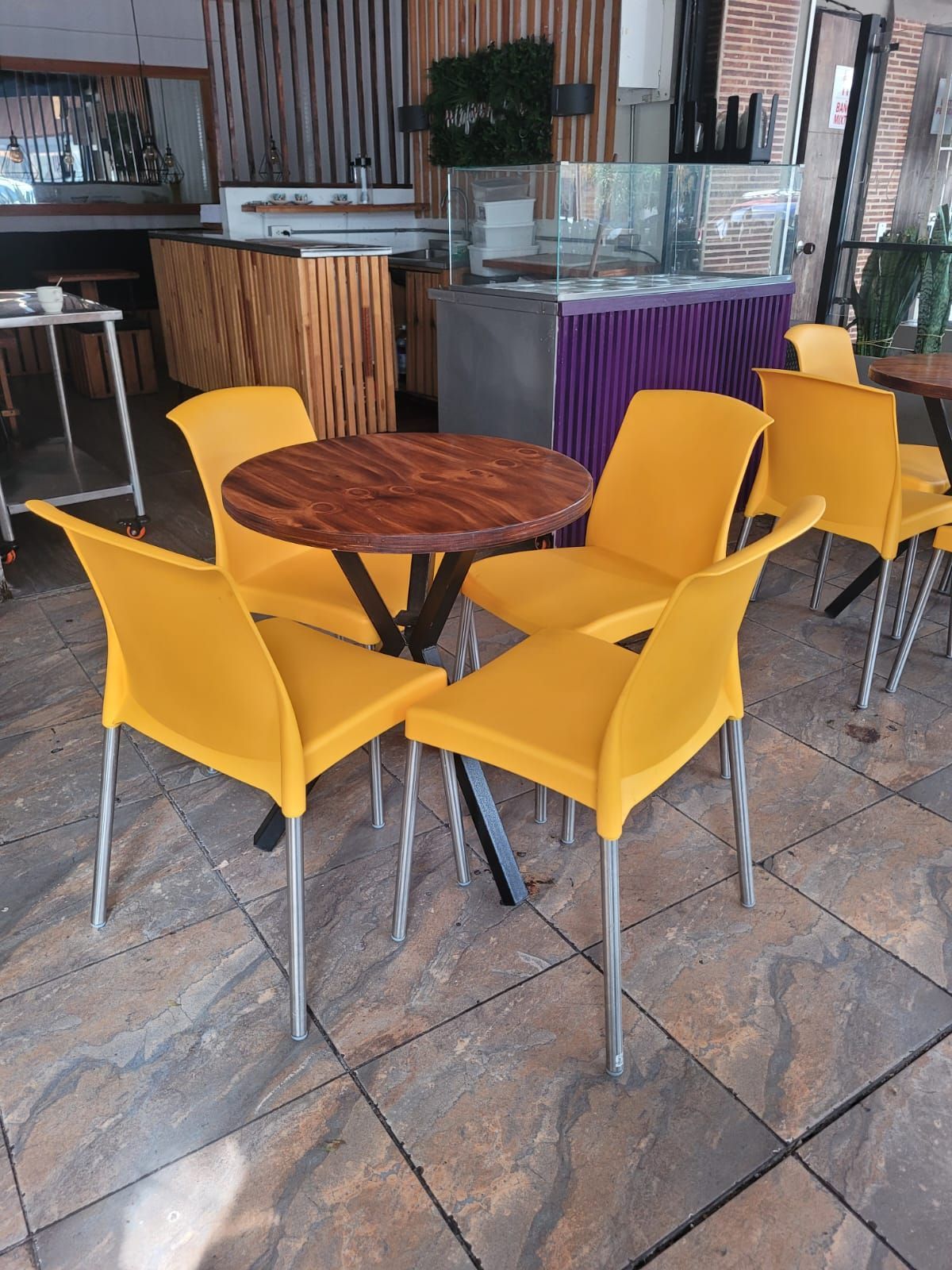 Sillas amarillas alrededor de una mesa redonda de madera en la zona de estar de una cafetería.