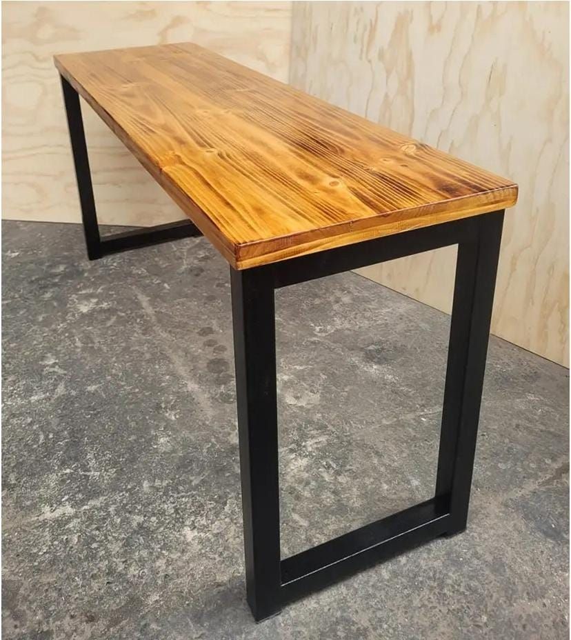 Mesa rústica con tablero de madera y patas de metal negro en un entorno de taller.