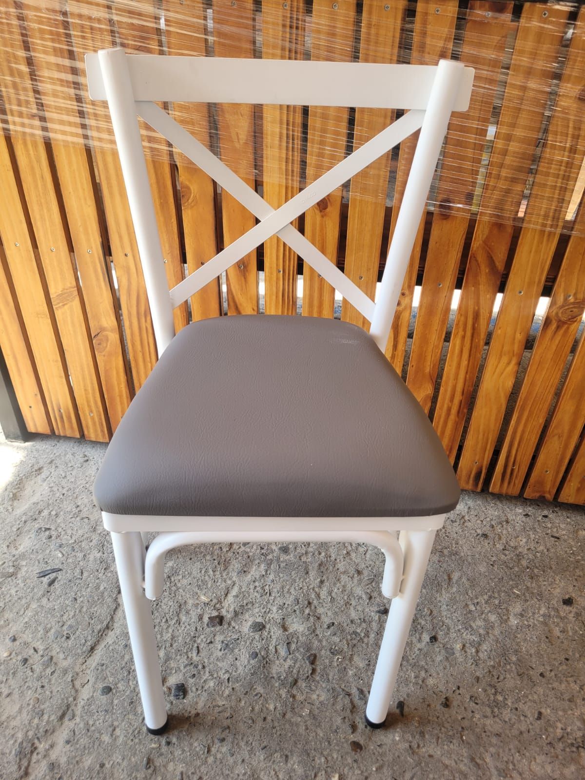 Silla de madera blanca con cojín gris sobre suelo de hormigón frente a una mampara de bambú.