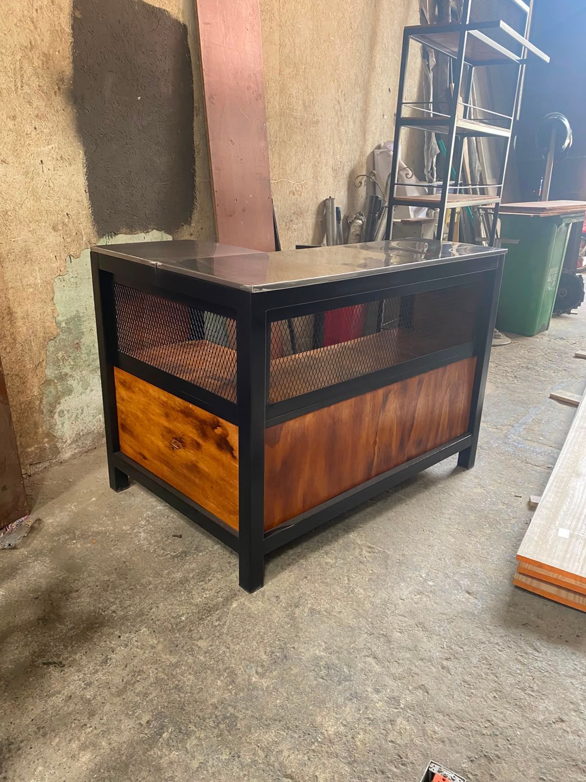 Estufa o calentador de exterior de metal negro y madera junto a una pared sobre un piso de concreto.