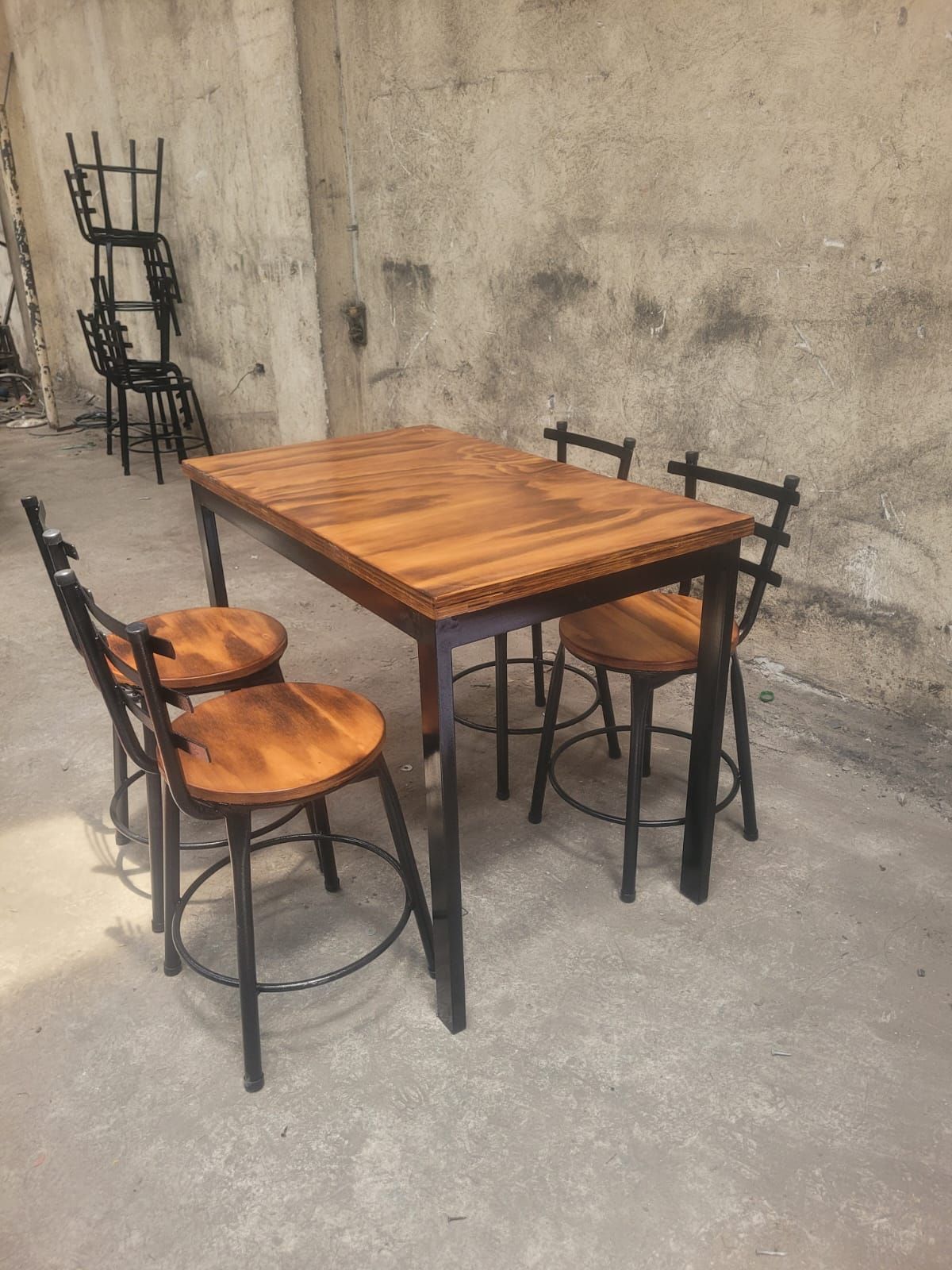 Mesa de madera con dos taburetes contra una pared de hormigón en un espacio interior austero.
