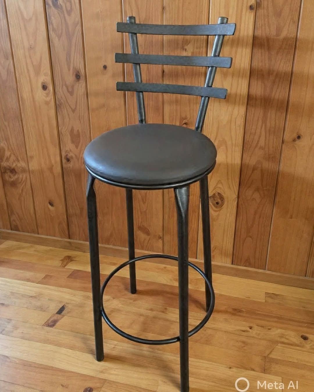 Taburete de bar de metal negro con asiento redondo, apoyado contra una pared revestida de madera.