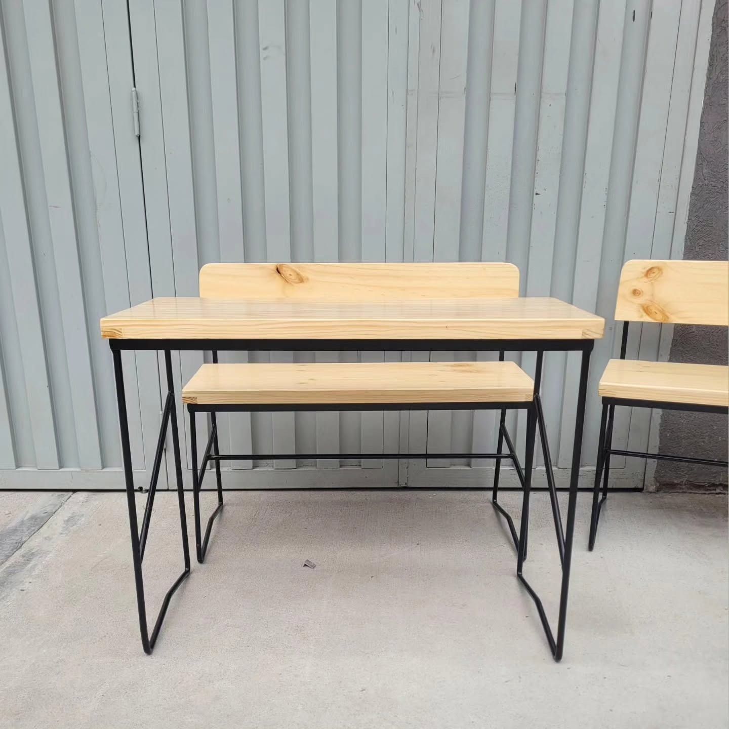 Dos mesitas de madera con patas de metal negro contra una pared corrugada gris sobre un suelo de hormigón.