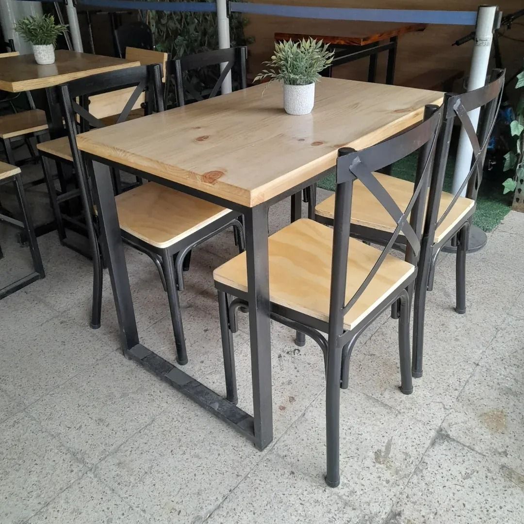 Mesa cuadrada de madera con cuatro sillas negras y una planta en maceta en la zona de estar de una cafetería.