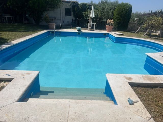 Piscina con tre sedie a sdraio, incorniciata da una siepe, con una casa in pietra e un villaggio sulla collina sullo sfondo.