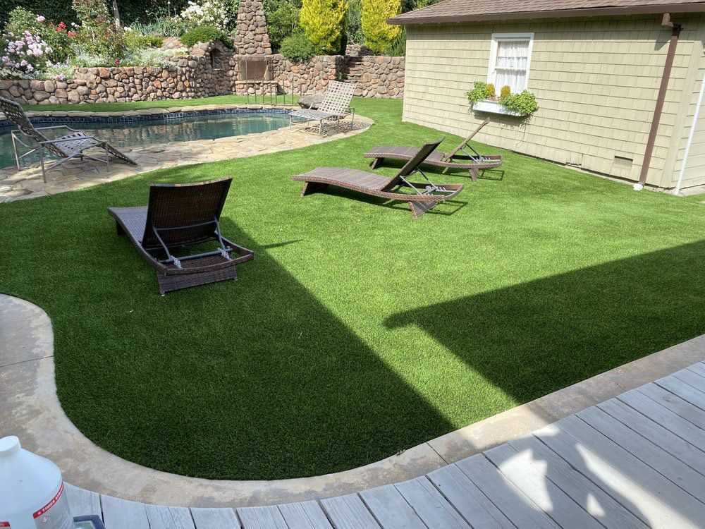 A backyard with a green lawn, three lounge chairs, a stone-edged pool, and a beige house.