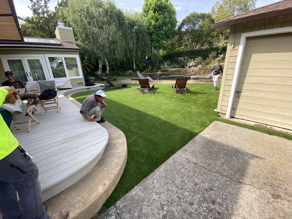 A backyard scene shows a white deck, a small lawn with lounge chairs, a person crouching, and another person walking.