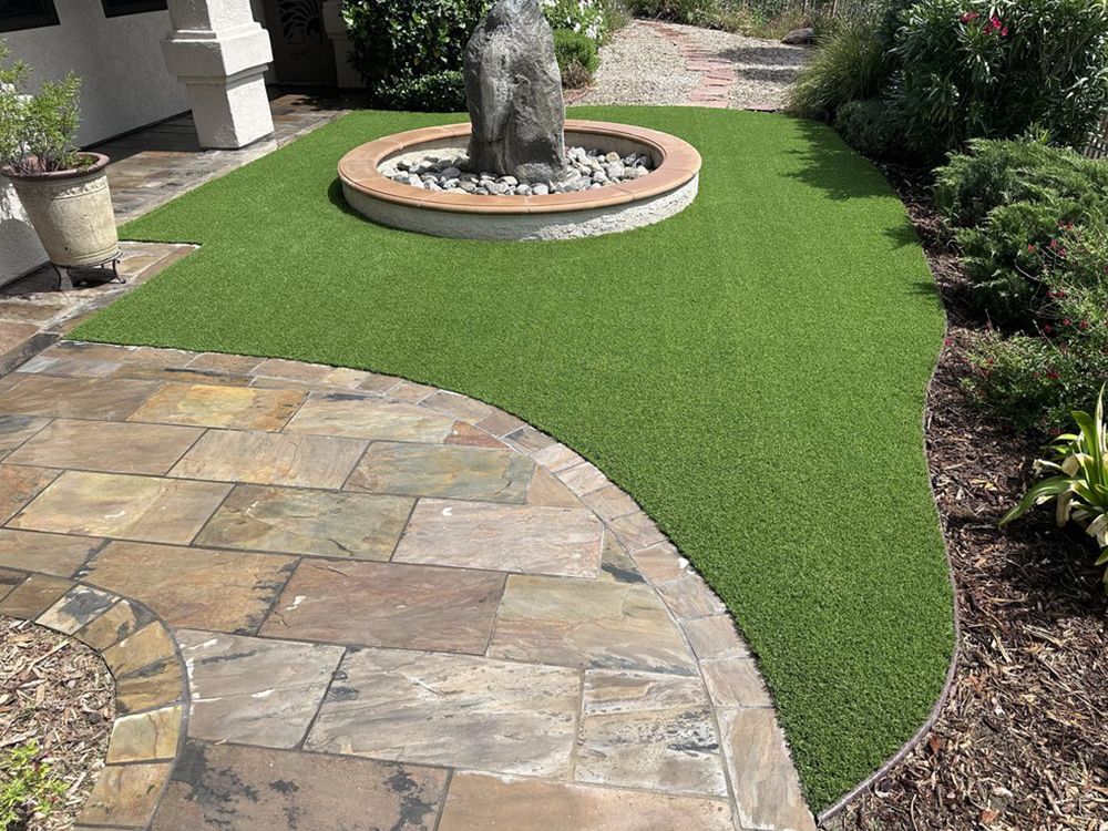 Stone patio with green artificial turf and a water fountain feature in a garden.