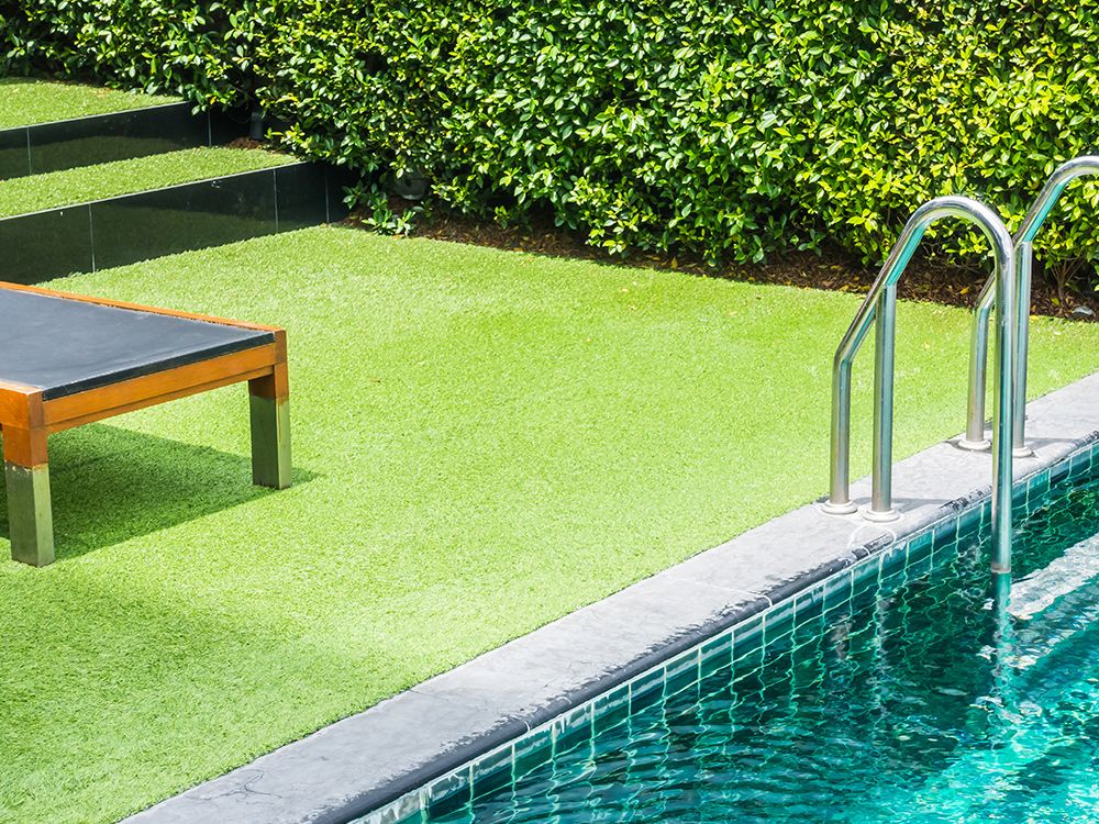Swimming pool with green turf, lounge chair, and a lush green hedge.