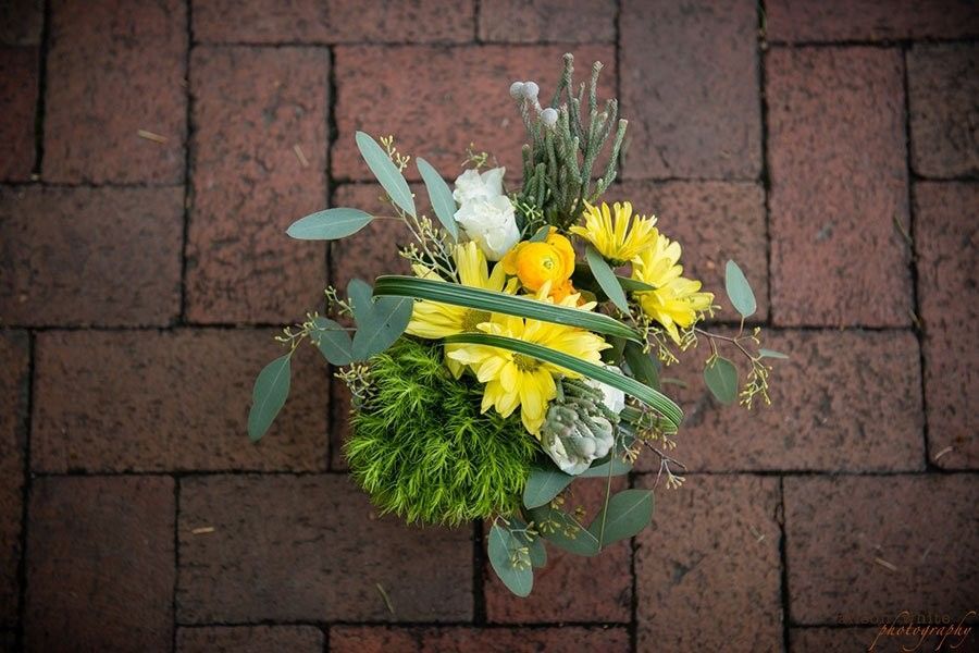 Small bouquet of yellow and white flowers with greenery on a red brick pavement