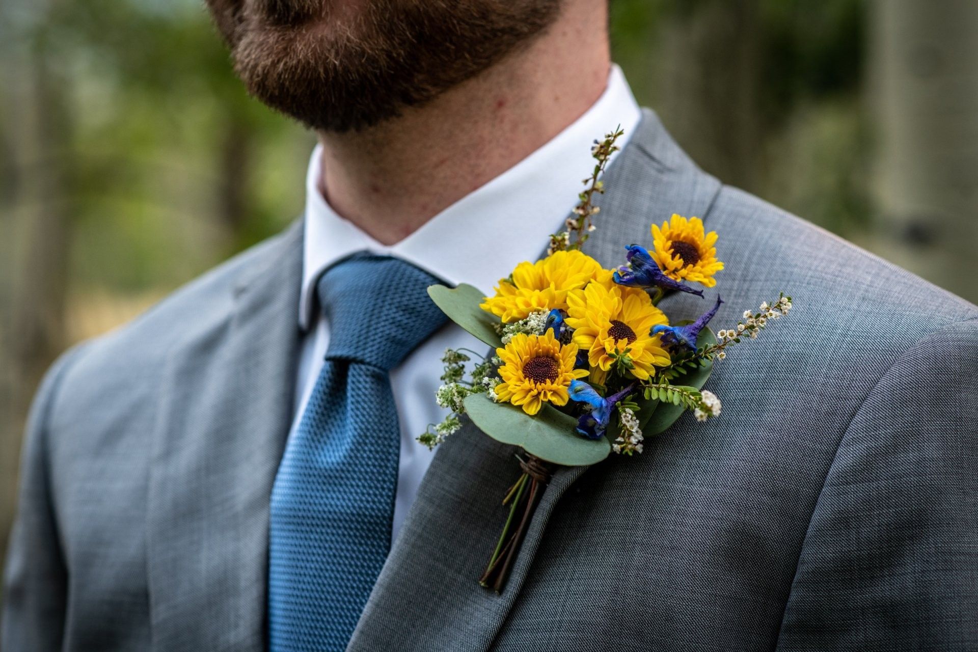 Gray suit with blue tie and yellow-blue boutonniere on lapel