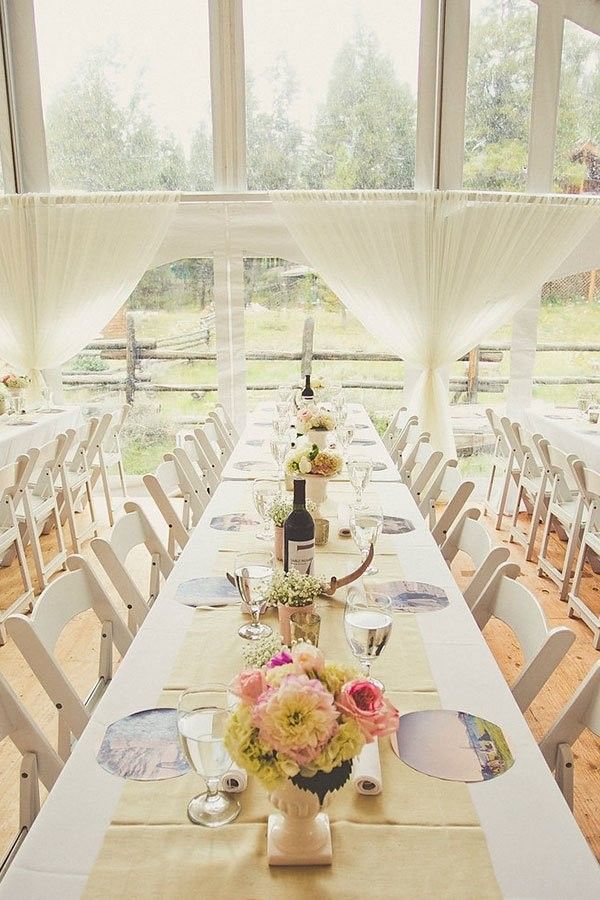 Elegant outdoor dining table set with white chairs, floral centerpieces, and bright windowed garden views