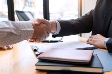 Businesspeople shaking hands over a desk with documents and a folder