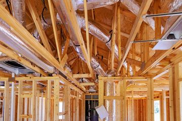 Exposed wooden framing and rafters inside a house under construction, with silver ductwork overhead