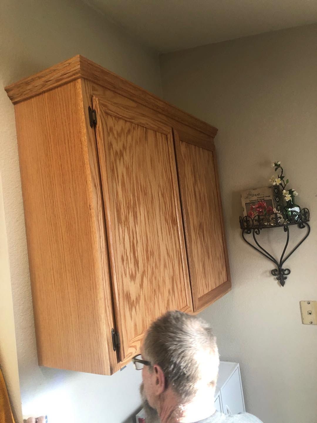Person looking into a kitchen cabinet beside a wall shelf and refrigerator.