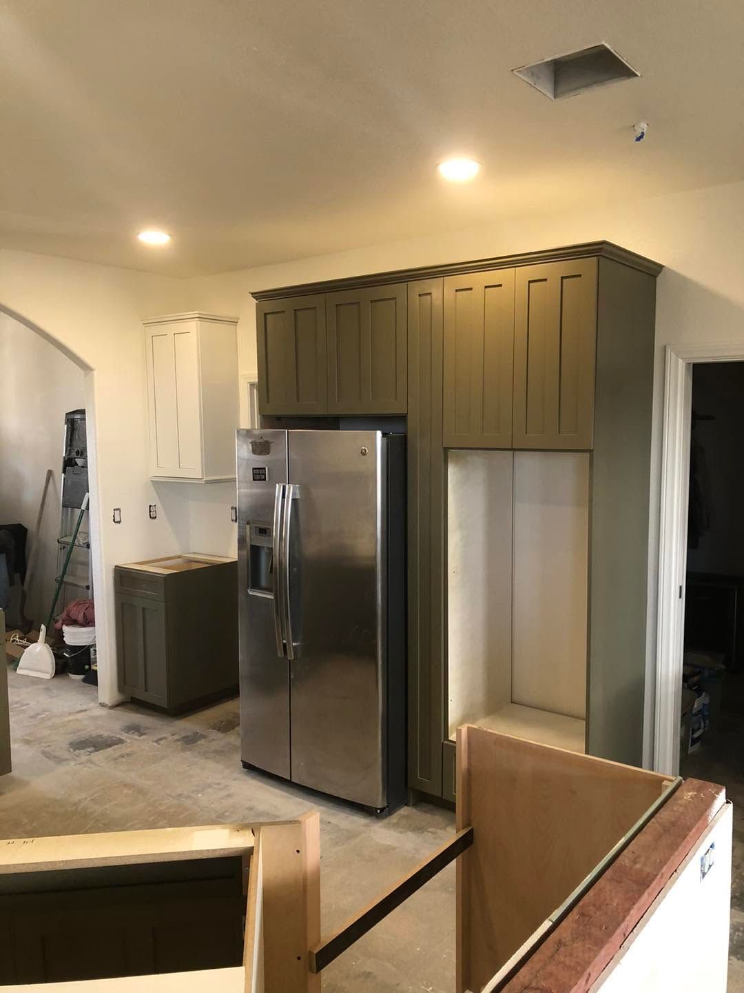 Modern kitchen with stainless steel refrigerator, olive cabinets, and a partially visible staircase.