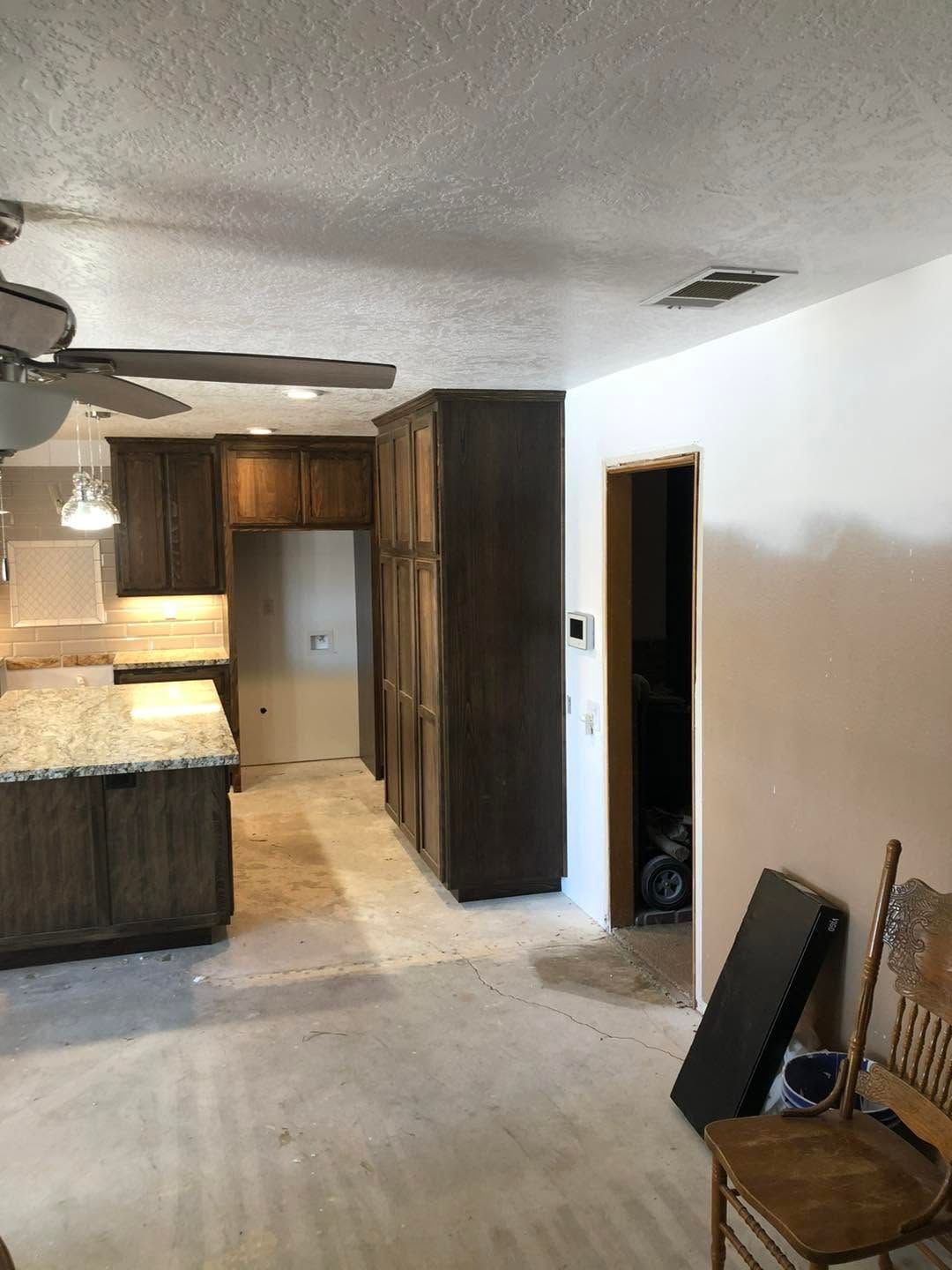 Empty kitchen with dark wood cabinets, white walls, ceiling fan, and a chair by the doorway.