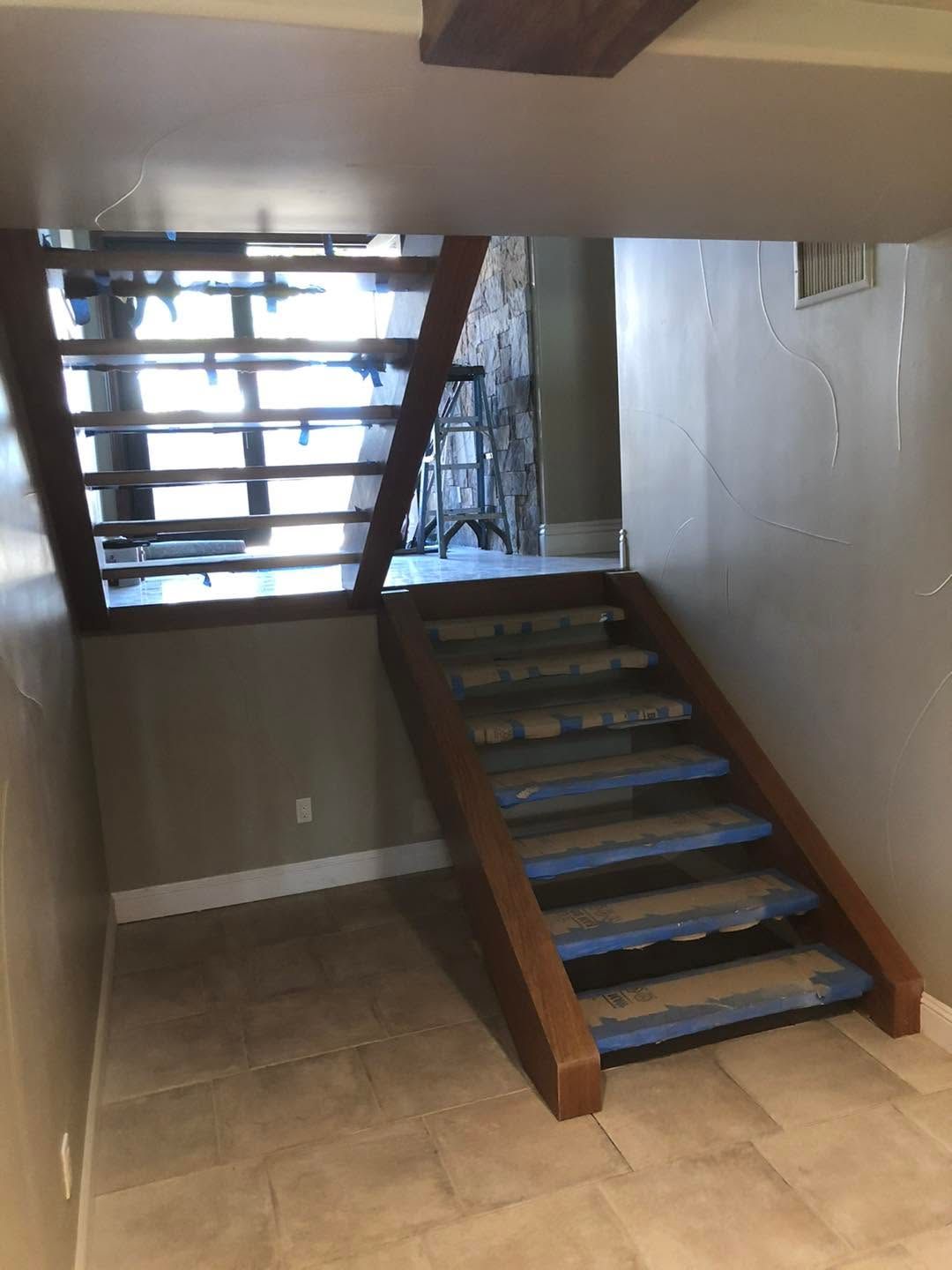 Indoor staircase with brown steps and metal railing in a tiled hallway beneath another stairway