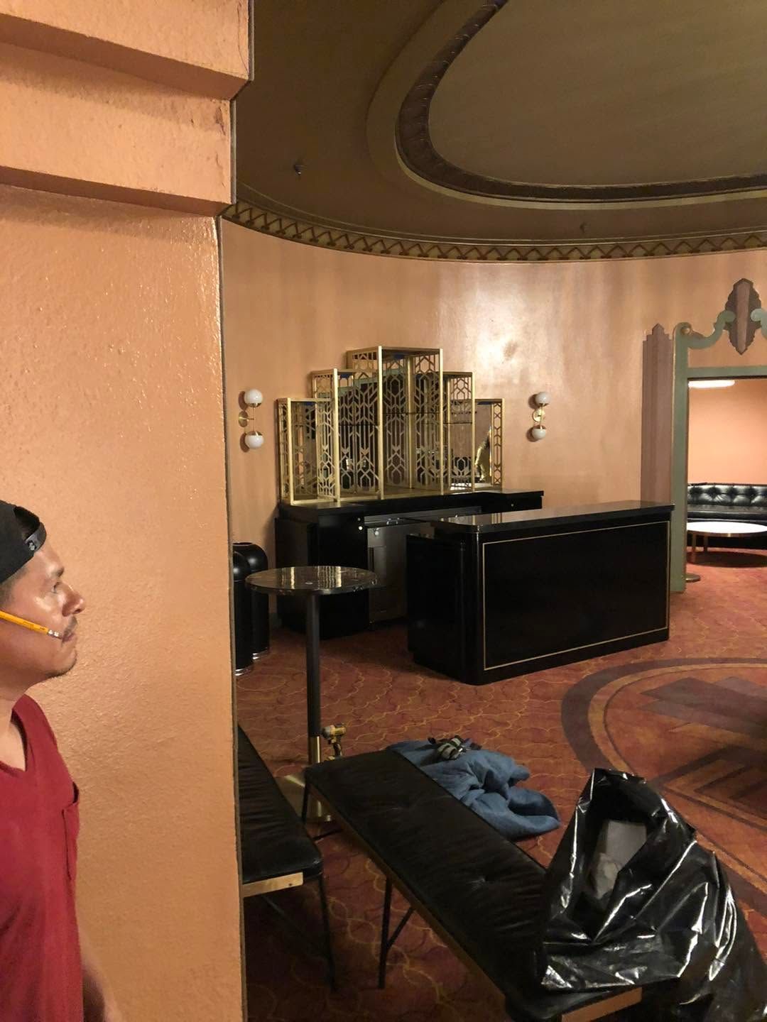 Hotel lobby with a black desk, decorative mirror, and a bench; a person stands at left edge.