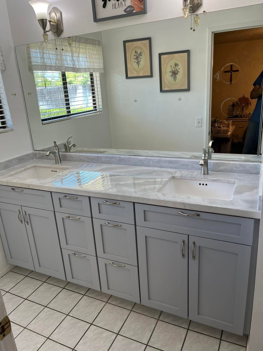 Bathroom vanity with double sinks, gray cabinets, white marble countertop, and wall mirror over tiled floor