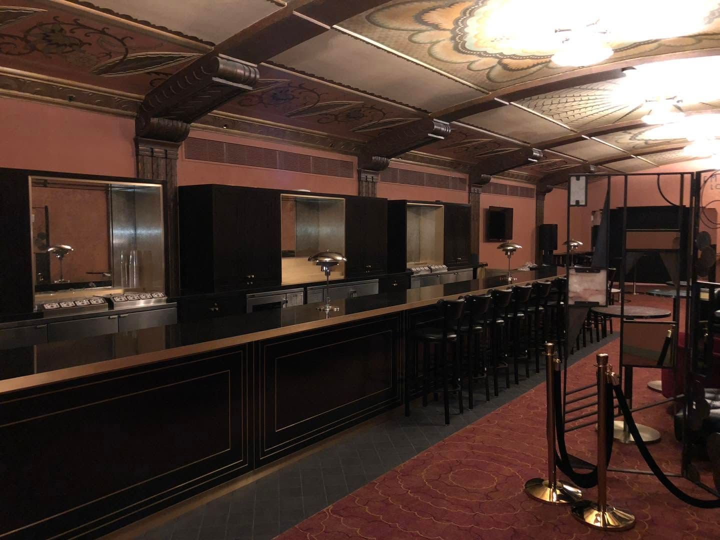 Empty bar with dark wood counter, high stools, and warm ceiling lights in a dim interior