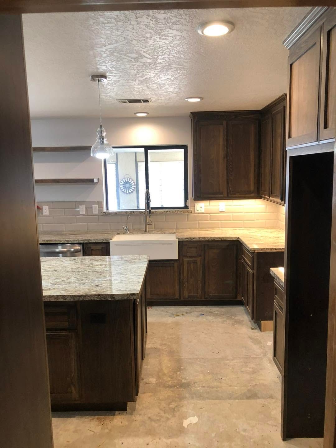 Empty kitchen with dark wood cabinets, light countertops, and a window over the sink.