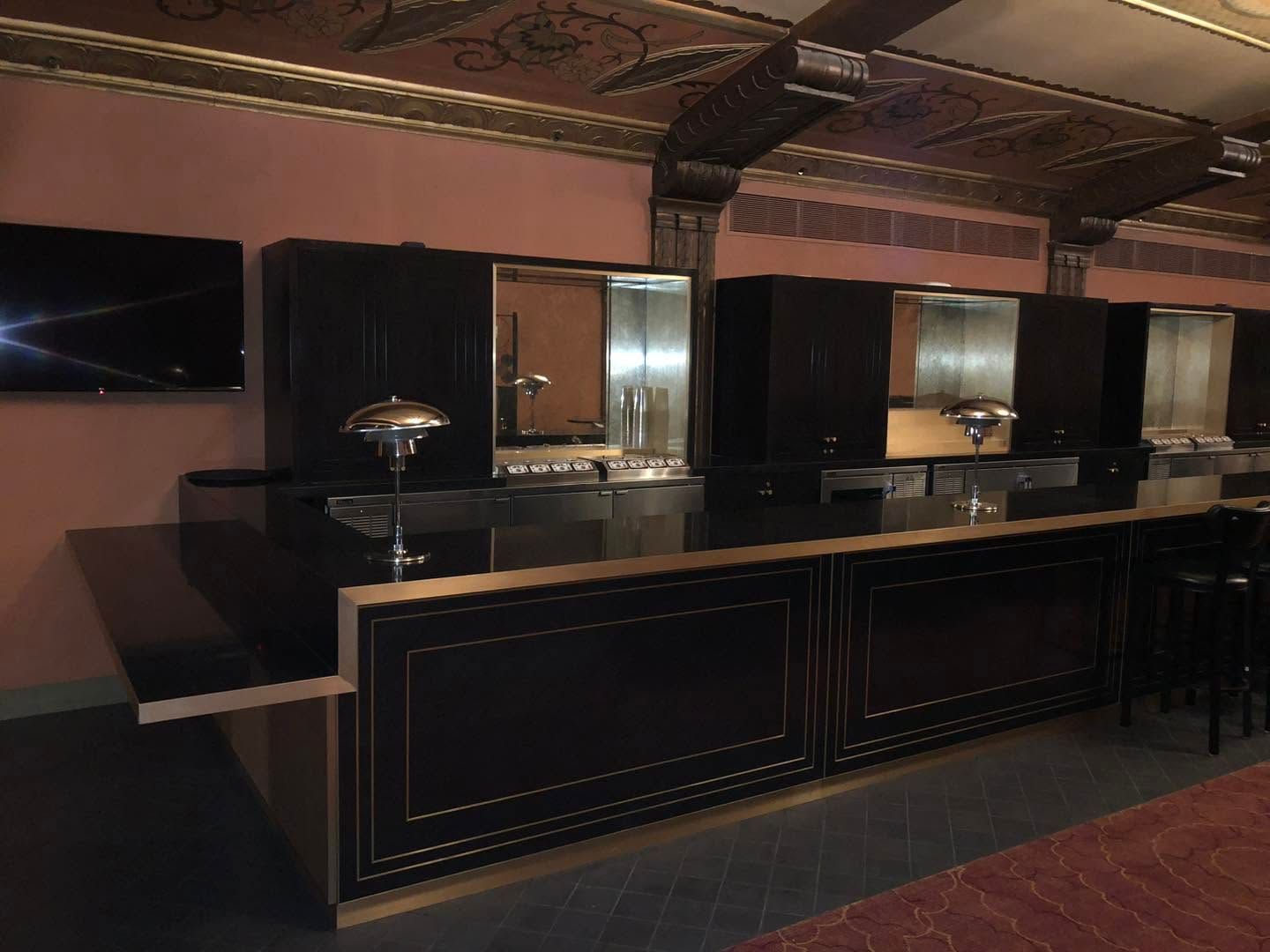 Dim bar counter in a dark, empty lounge with black panels and mirrored shelves under ornate ceiling beams