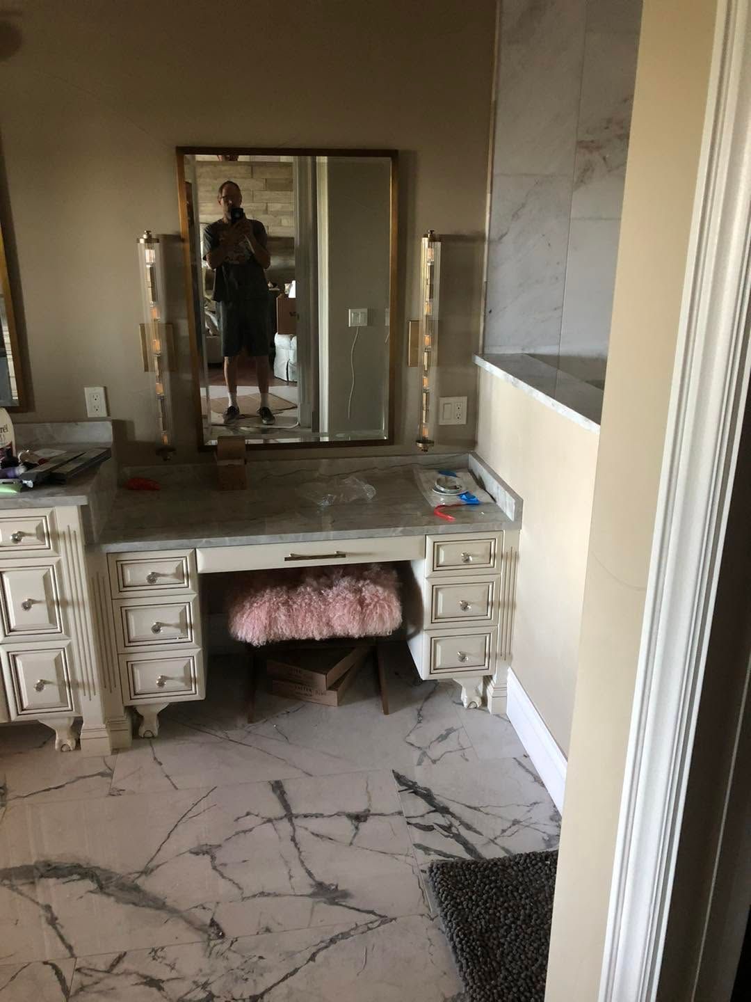 Bathroom vanity with mirror, white drawers, marble-style floor, and a person visible in the mirror.