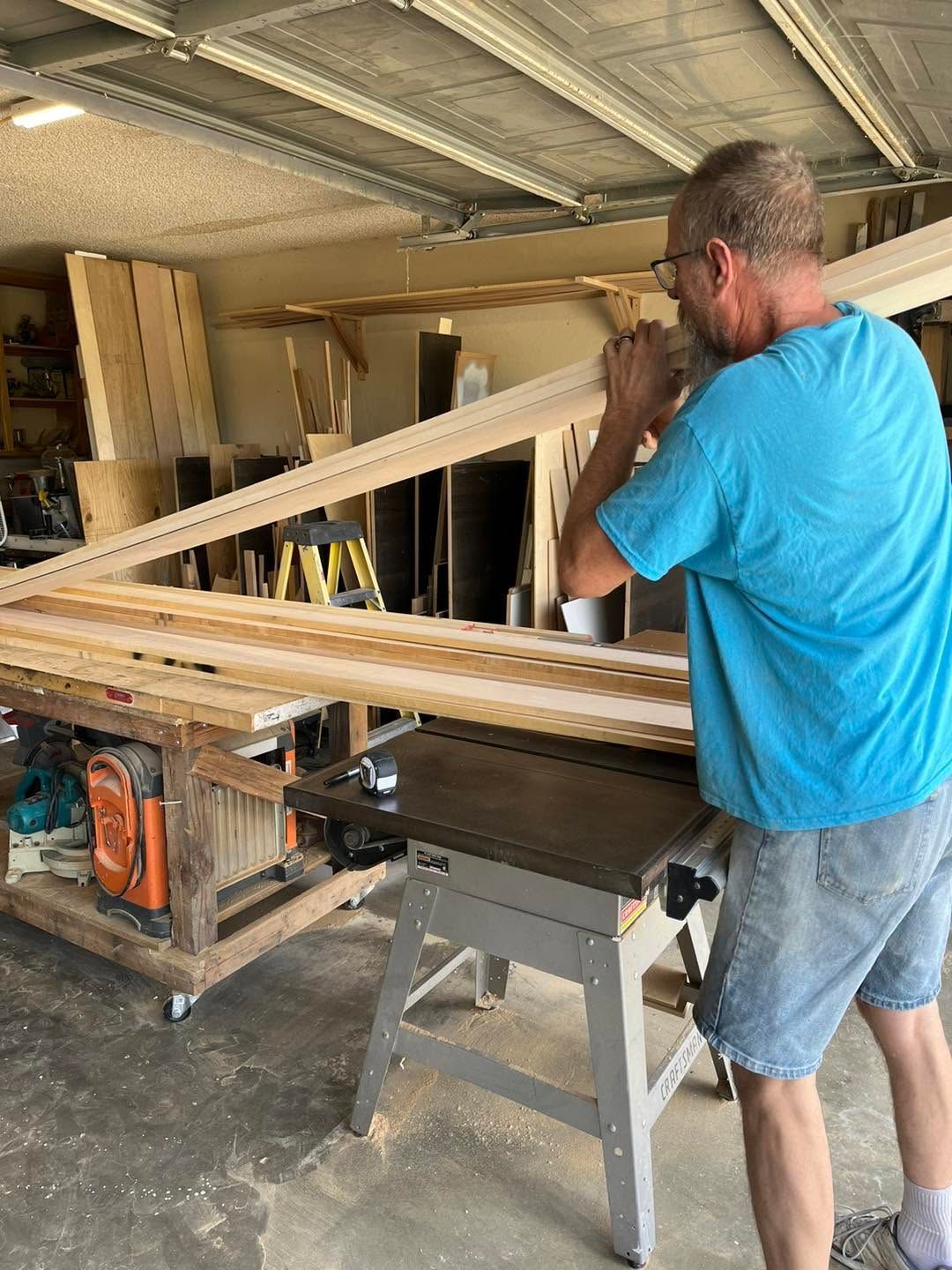 Man in a blue shirt using a table saw to cut long boards in a workshop