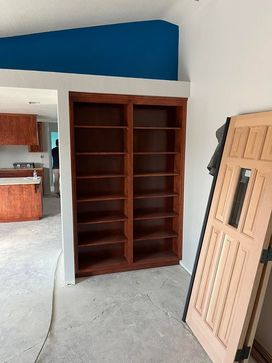 Wooden built-in shelves beside a doorway in a room with a blue accent wall, with a door leaning nearby.