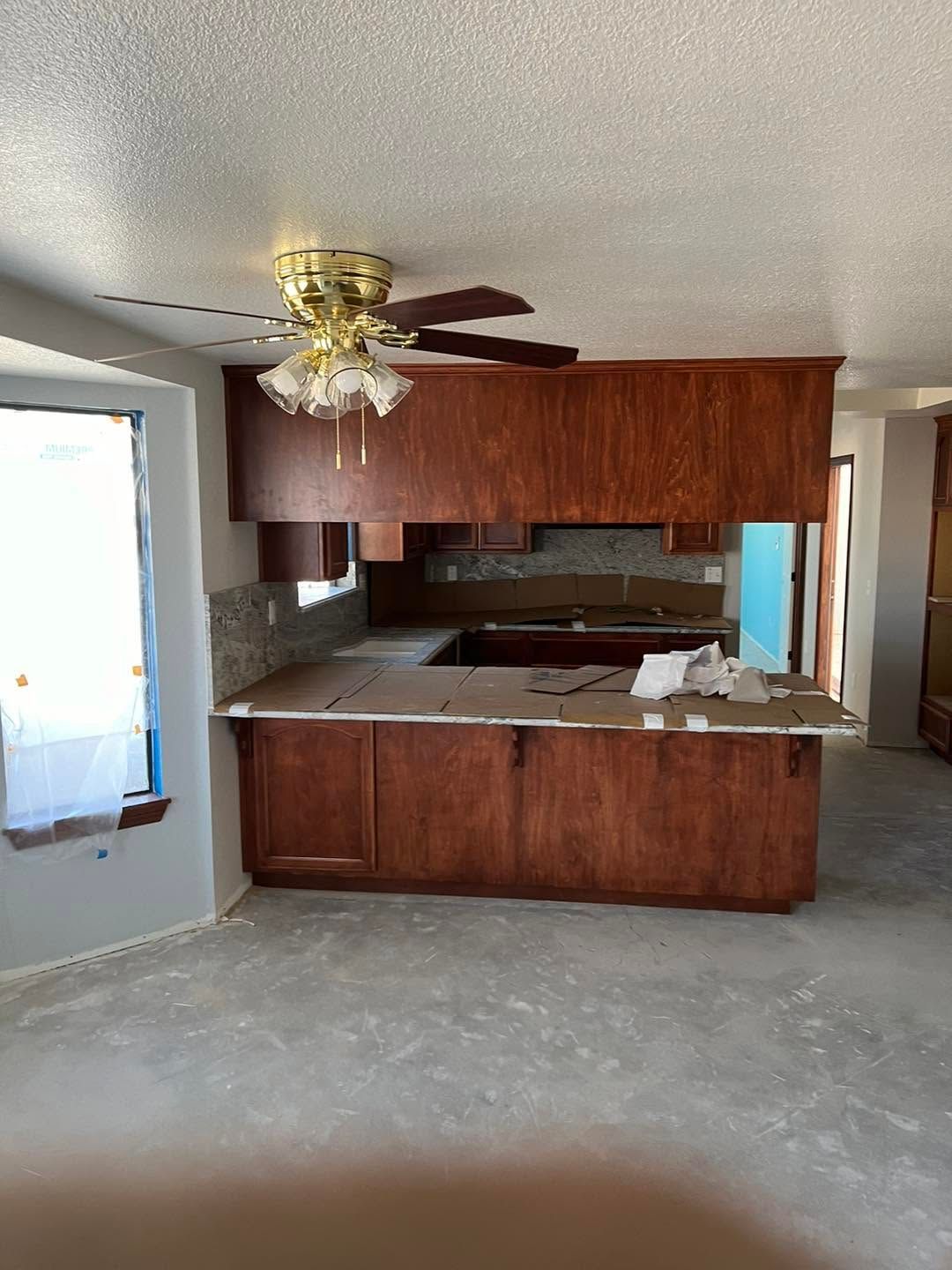 Small kitchen with wood cabinets, white countertops, and a ceiling fan in a sparse room.