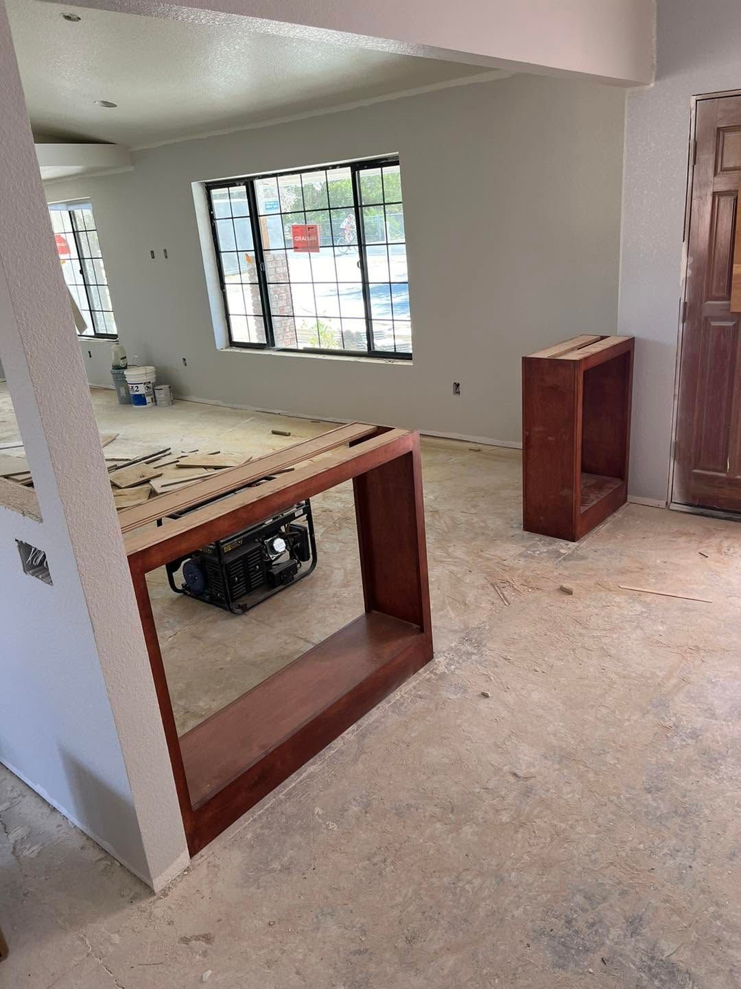 Unfinished room with a wooden counter frame, cabinet, and large windows letting in daylight.