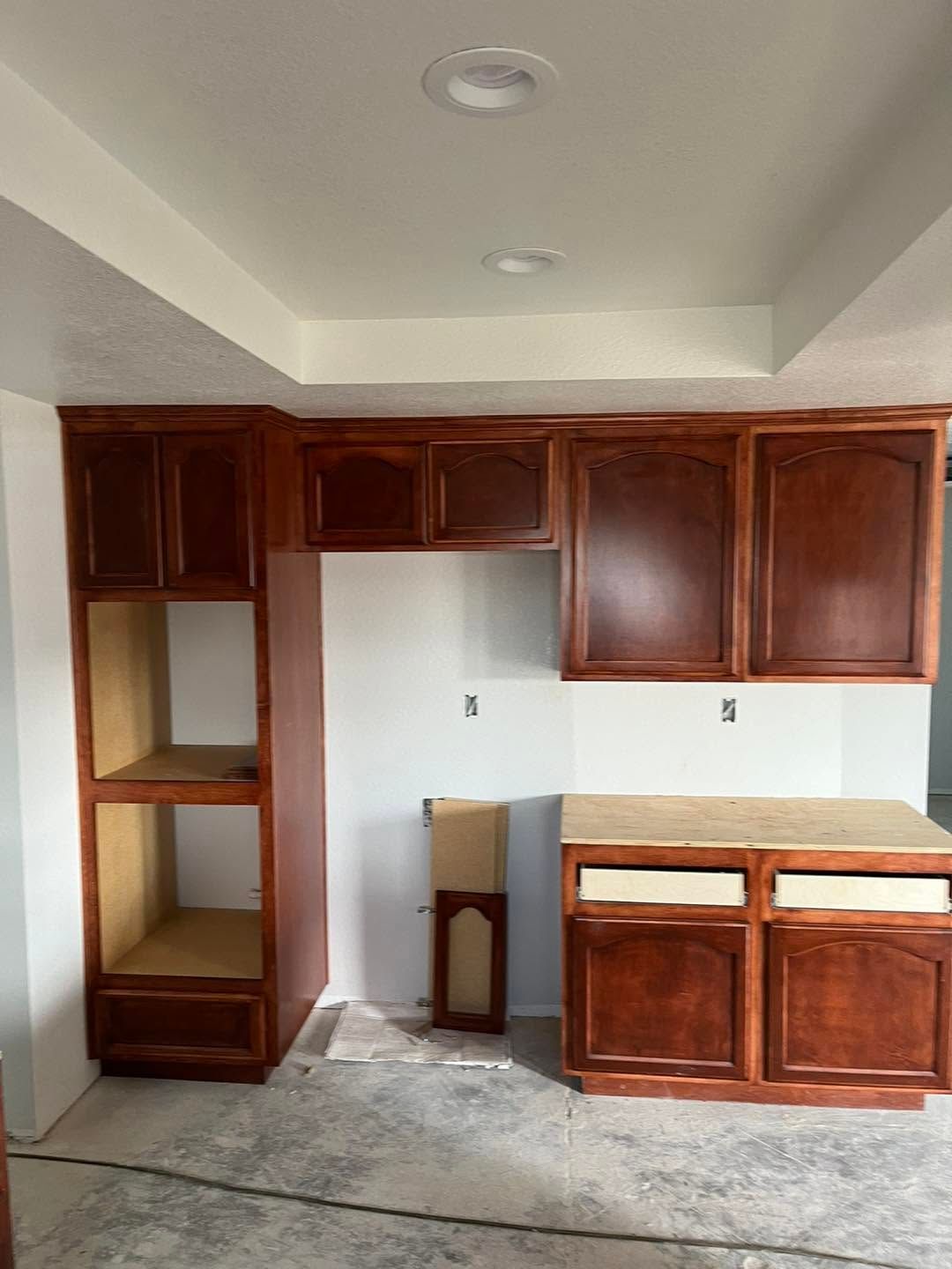 Empty kitchen with dark wood cabinets, white walls, and unfinished concrete floor